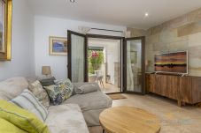 Salón acogedor con sofá esquinero, mesa de madera y puertas acristaladas que conectan con una terraza llena de plantas.