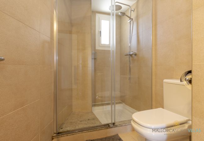 Baño con ducha de cristal y luz natural en Pollensa Ducha de cristal con rociador efecto lluvia y ventana en baño moderno