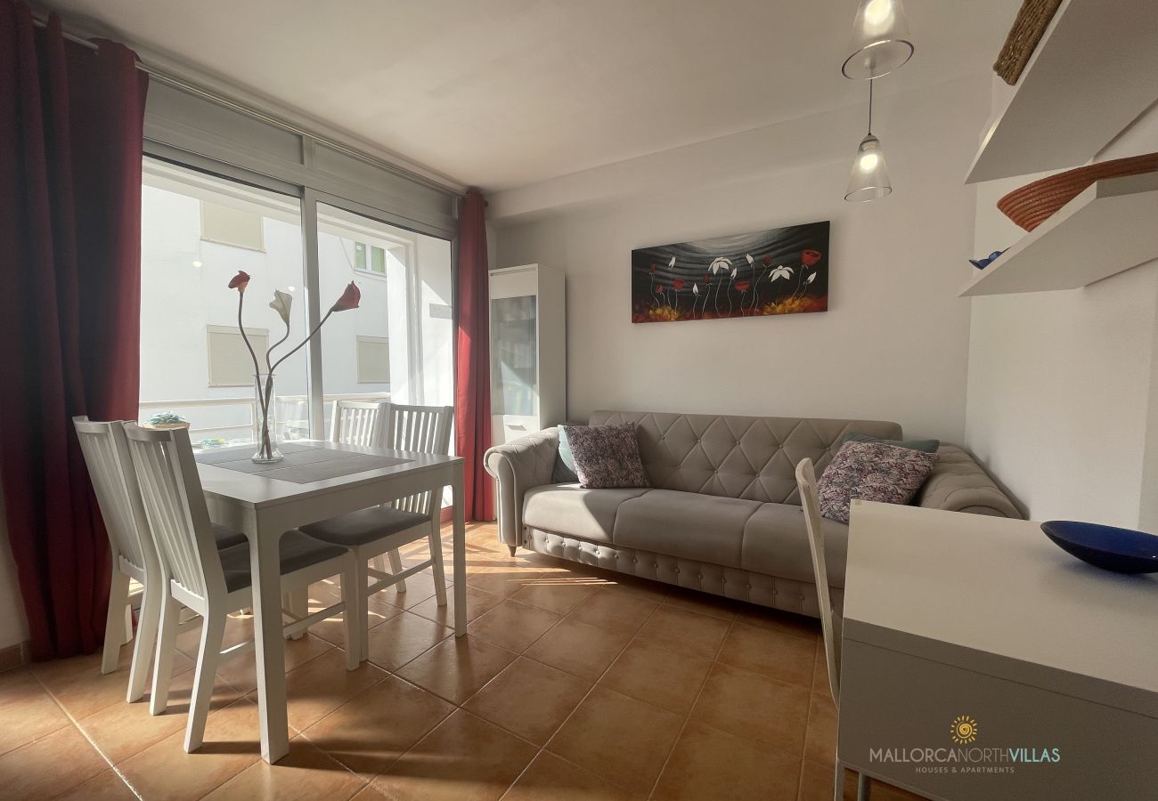Apartamento Aurora 3 – Salón comedor luminoso con sofá y mesa Salón comedor con sofá gris, mesa blanca para cuatro y gran ventanal en el Apartamento Aurora 3