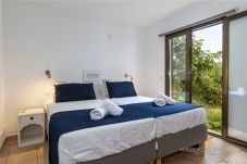 Chambre lumineuse avec deux lits réunis, linge de lit bleu et porte coulissante ouvrant sur le jardin.